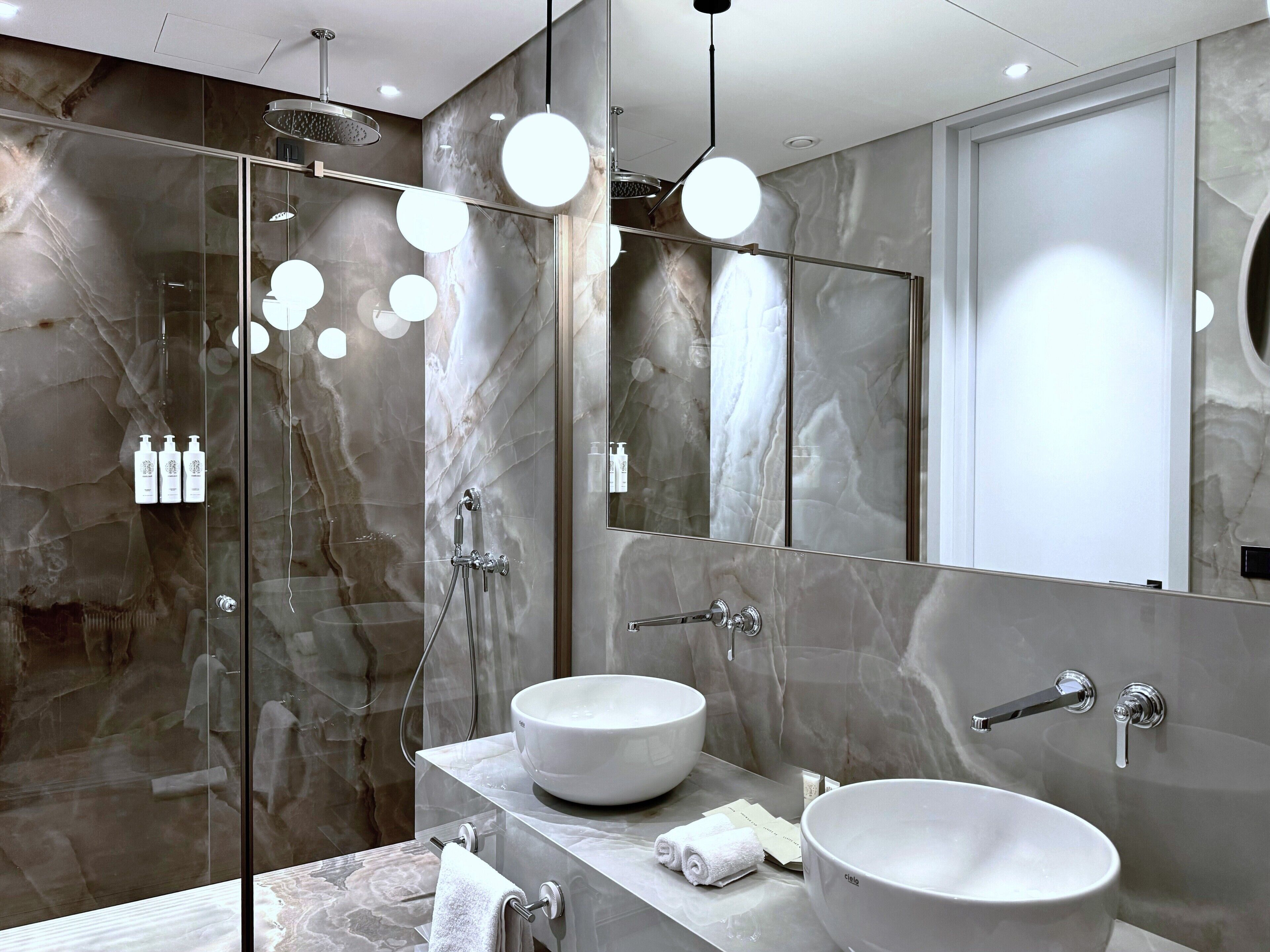 A modern bathroom with two large white sinks, a glass-enclosed shower, and a large mirror.