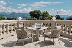 Una terraza con sillones de mimbre, una mesa redonda y vistas a las montañas y al agua.