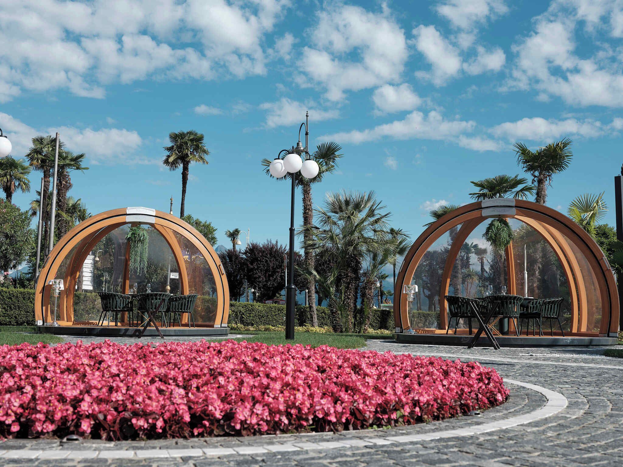 Two transparent dome structures with seating inside, surrounded by a landscaped garden with pink flowers.