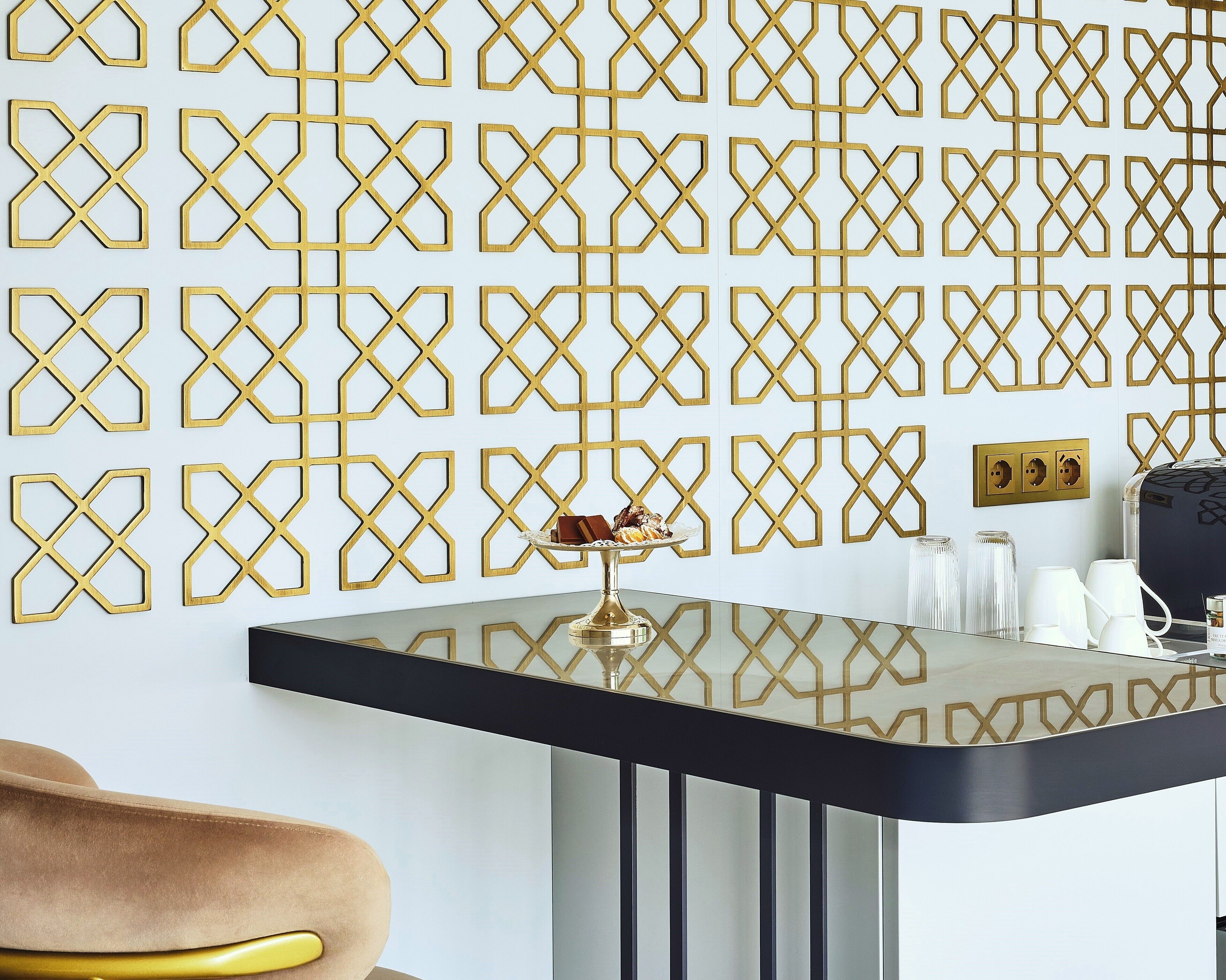 A modern room with a geometric patterned wall, a black table with a gold base, and a brown chair.