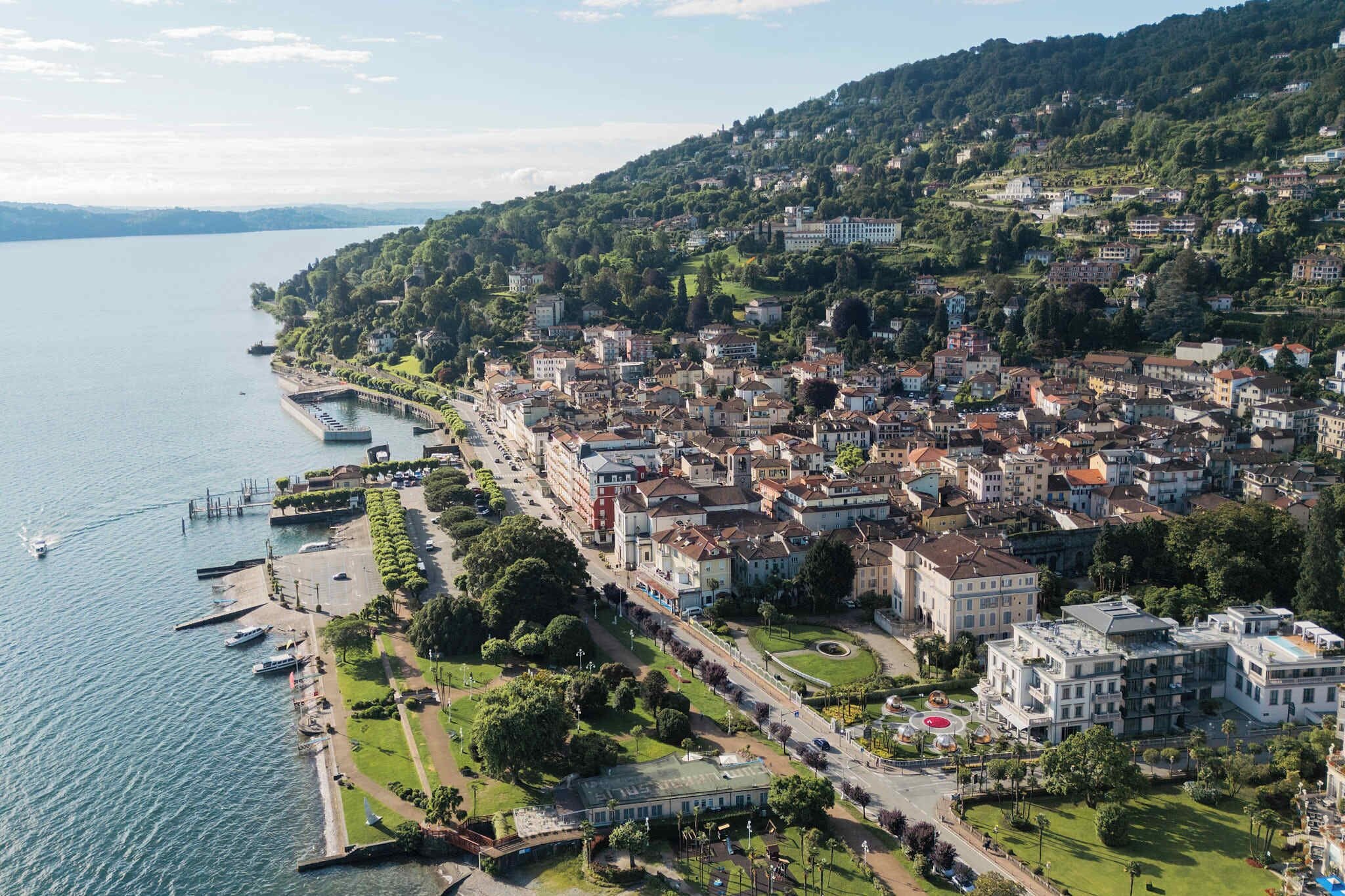 An aerial view of a coastal town with buildings, a marina, and a hill with greenery.