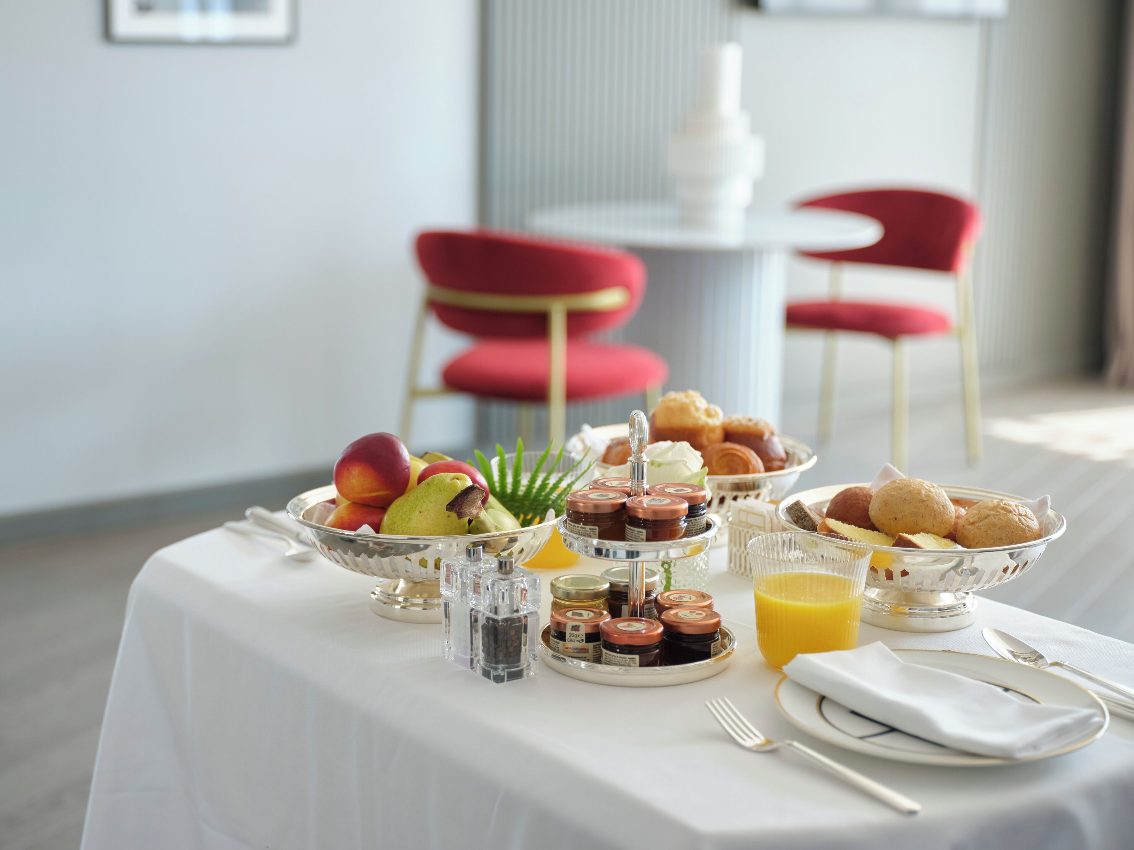 A breakfast table with fruits, pastries, condiments, and a glass of orange juice.