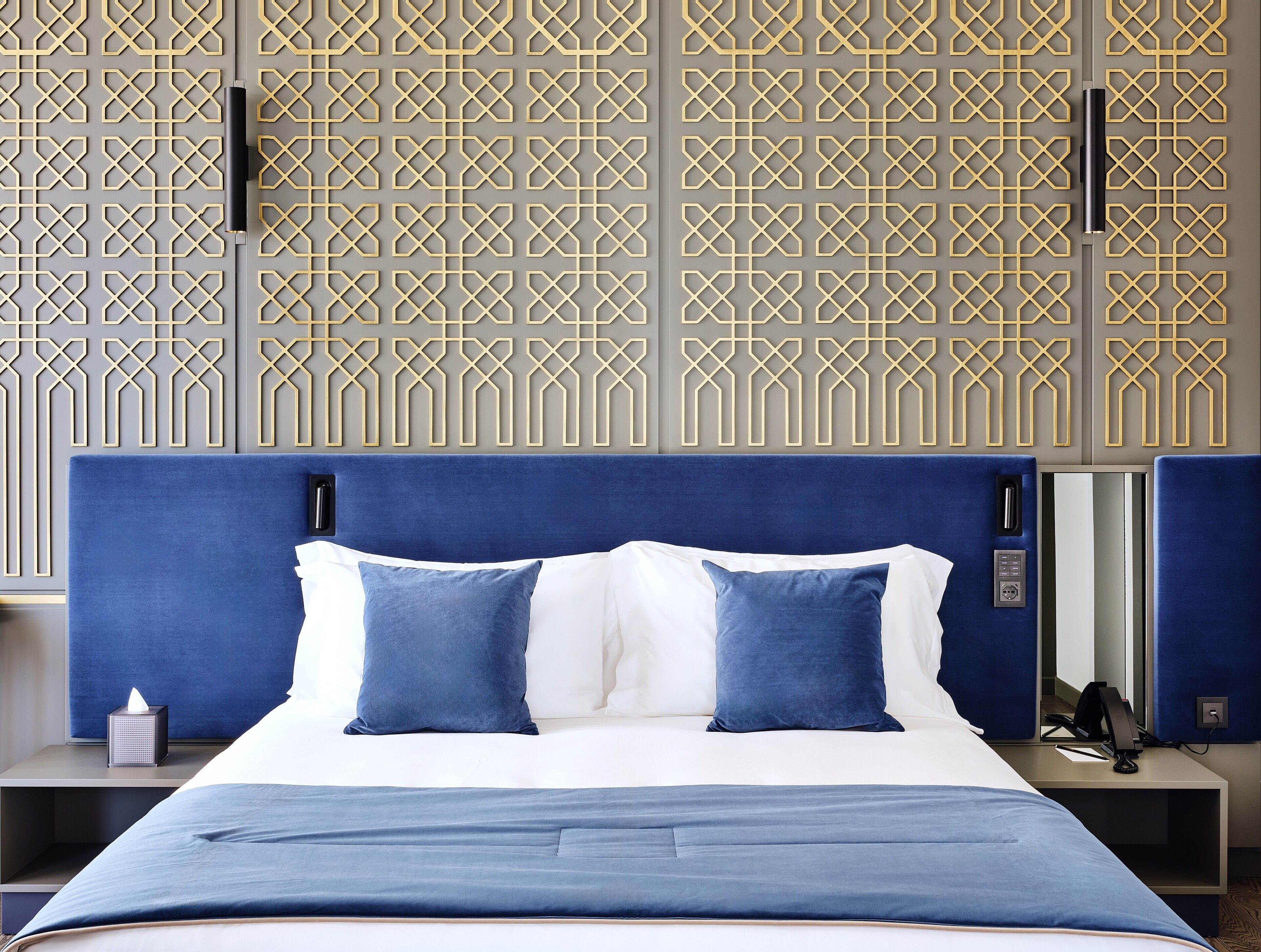 Une chambre d’hôtel avec un lit, une table de chevet, un bureau et un mur orné d’un motif géométrique.