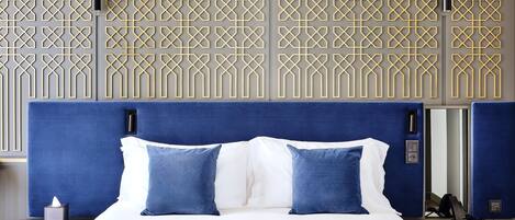 Une chambre d’hôtel avec un lit, une table de chevet, un bureau et un mur orné d’un motif géométrique.
