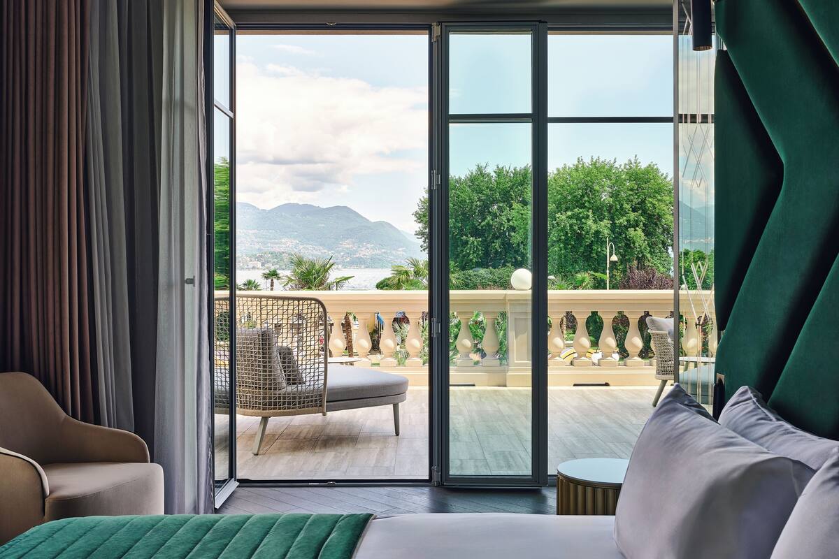 Une chambre d’hôtel avec un lit, une chaise et un balcon offrant une vue sur les montagnes et la verdure.