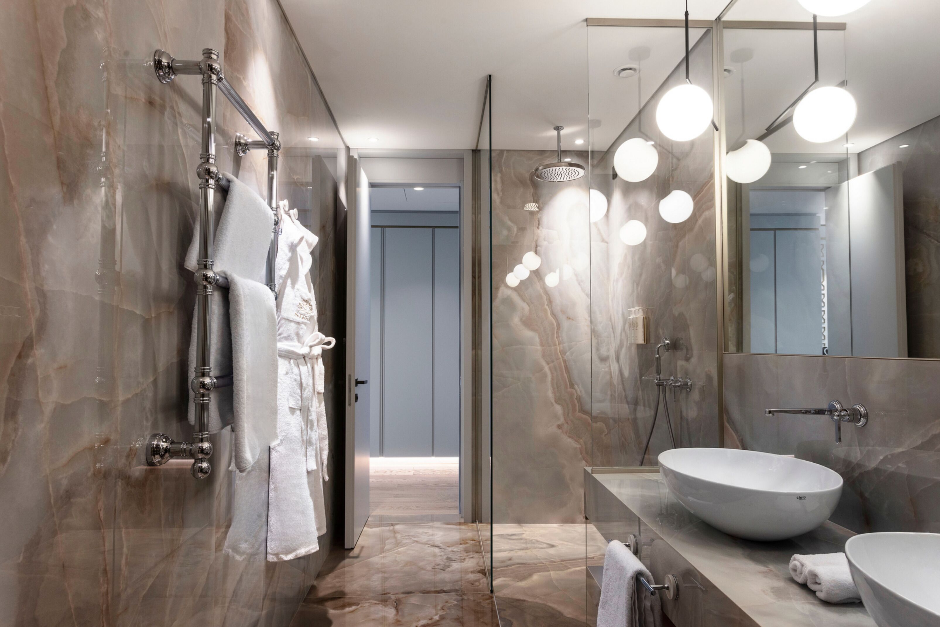 Une salle de bain moderne avec un grand miroir, un lavabo sur colonne et une douche à parois de verre.