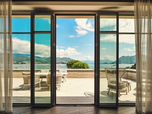 A view through a glass door to an outdoor seating area with wicker chairs and a wooden deck. - Boutique Hotel Stresa (Stresa)
