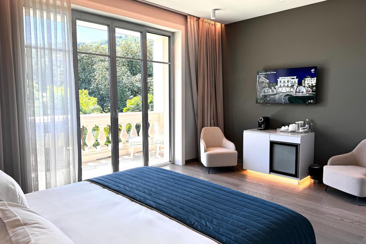 Une chambre d’hôtel dotée d’un grand lit, d’un bureau avec une machine à café, d’un téléviseur fixé au mur et d’un balcon aménagé avec du mobilier d’extérieur.
