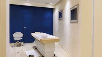 Une salle d’examen médical avec un mur bleu, une table d’examen blanche, une chaise blanche et un tableau encadré accroché au mur.