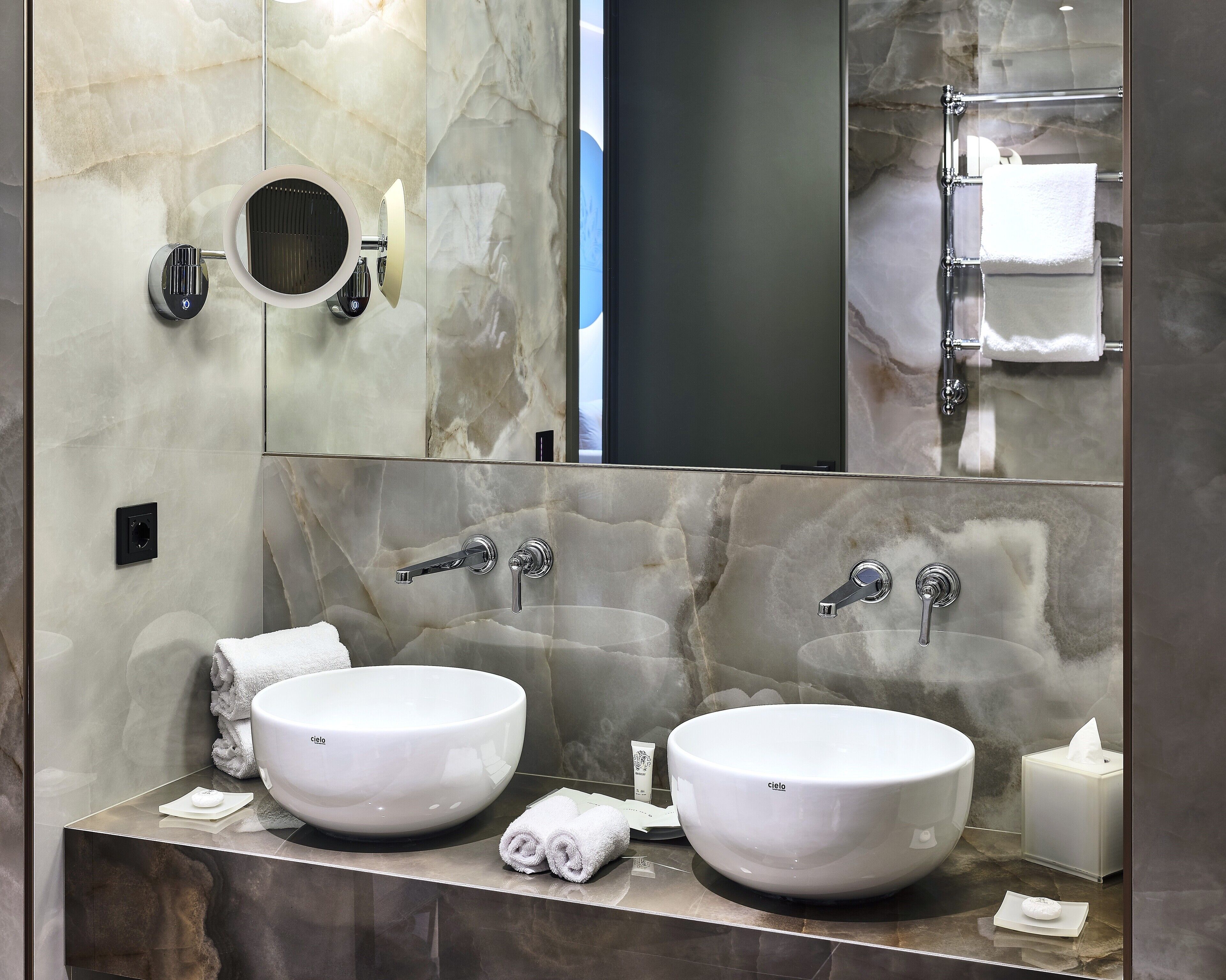 Un bagno con due lavandini bianchi, un grande specchio e un portasciugamani.