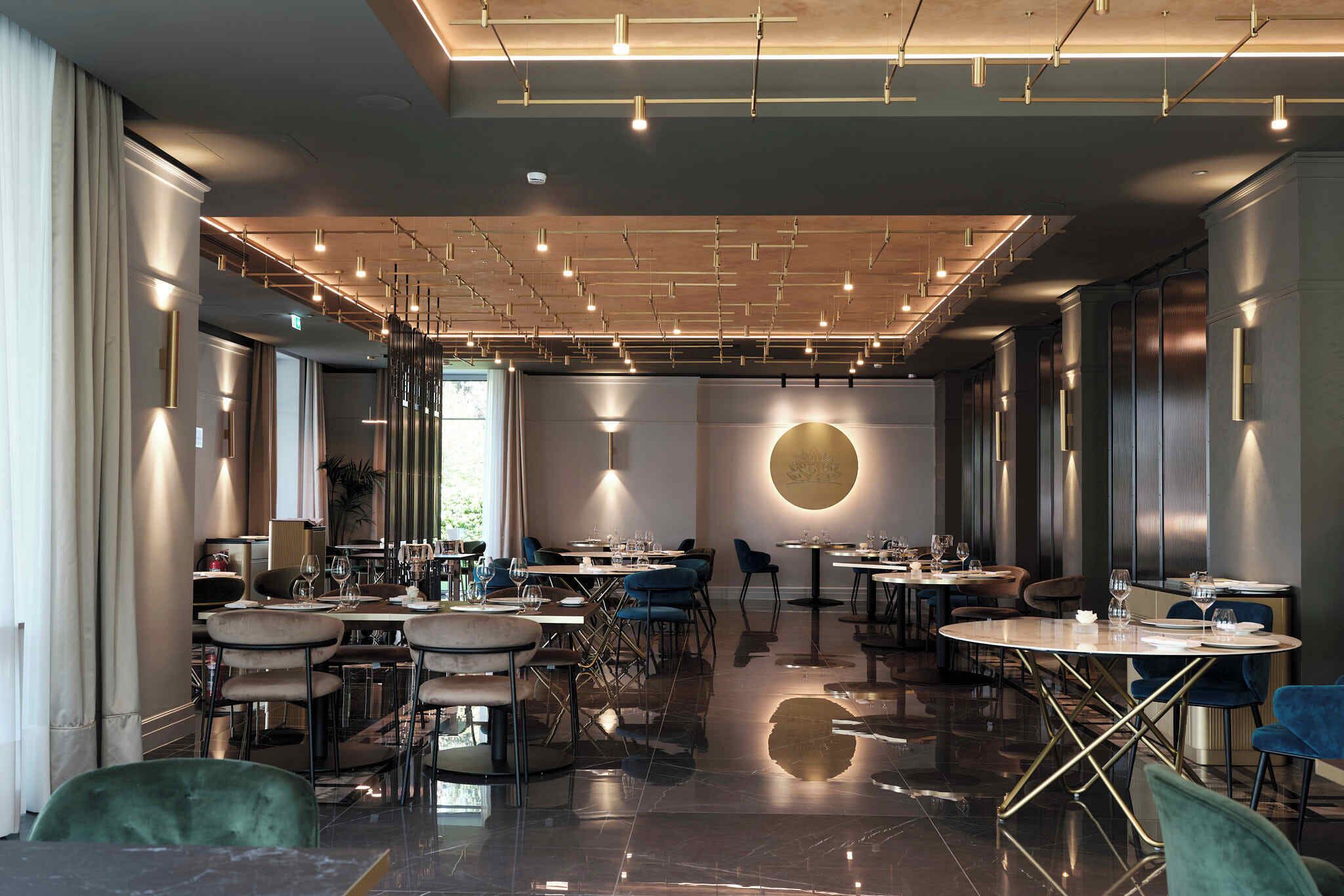 Un restaurant moderne doté de nombreuses tables et chaises, d’un sol en marbre poli et d’un plafond agrémenté de luminaires linéaires.