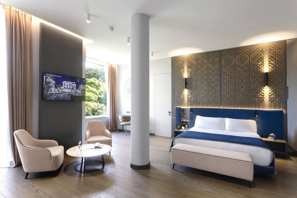 Une chambre d’hôtel moderne dotée d’un grand lit, d’un téléviseur fixé au mur, d’un coin salon avec une table et d’un panneau décoratif mural.