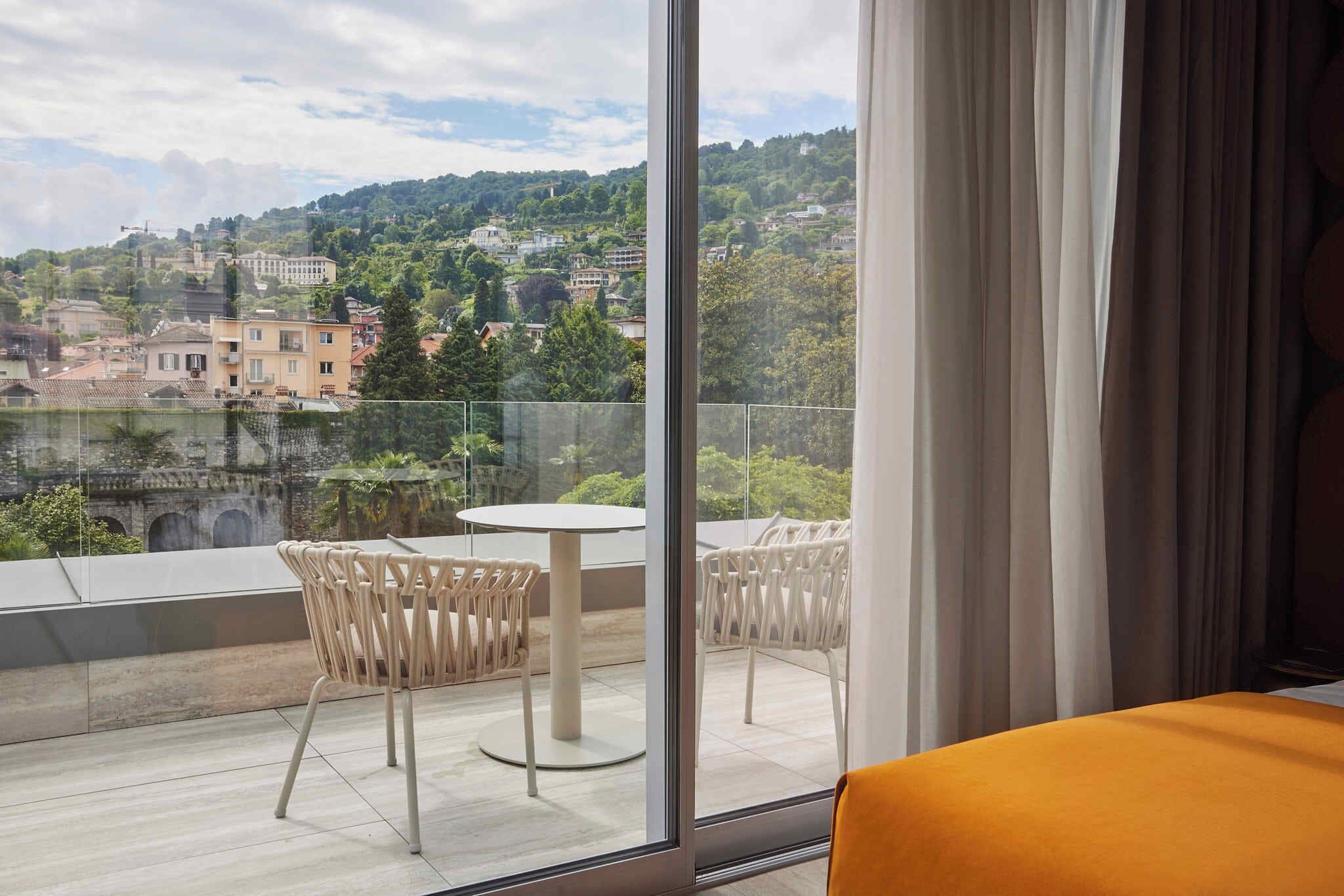 A hotel room with a balcony overlooking a scenic view of a town and hills.