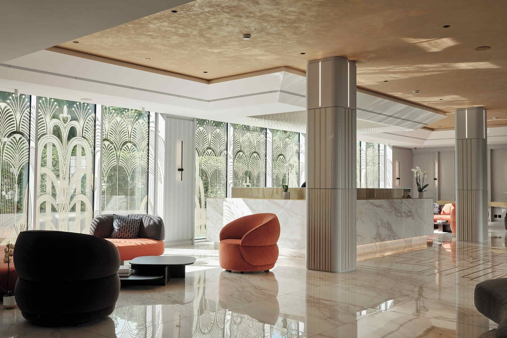 A spacious lobby with a marble floor, modern seating, and large windows with decorative patterns.