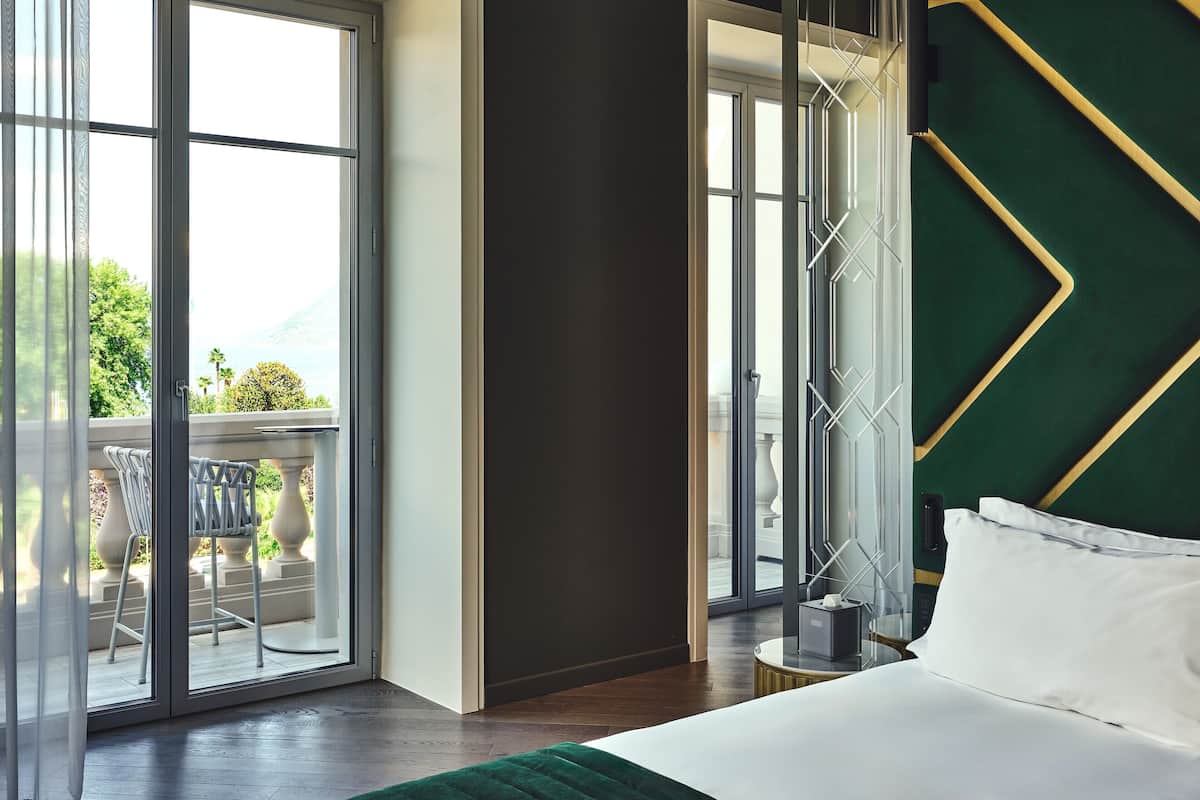 Une chambre d’hôtel moderne dotée d’un grand lit, d’un balcon avec mobilier d’extérieur et offrant une vue sur la verdure et les montagnes.