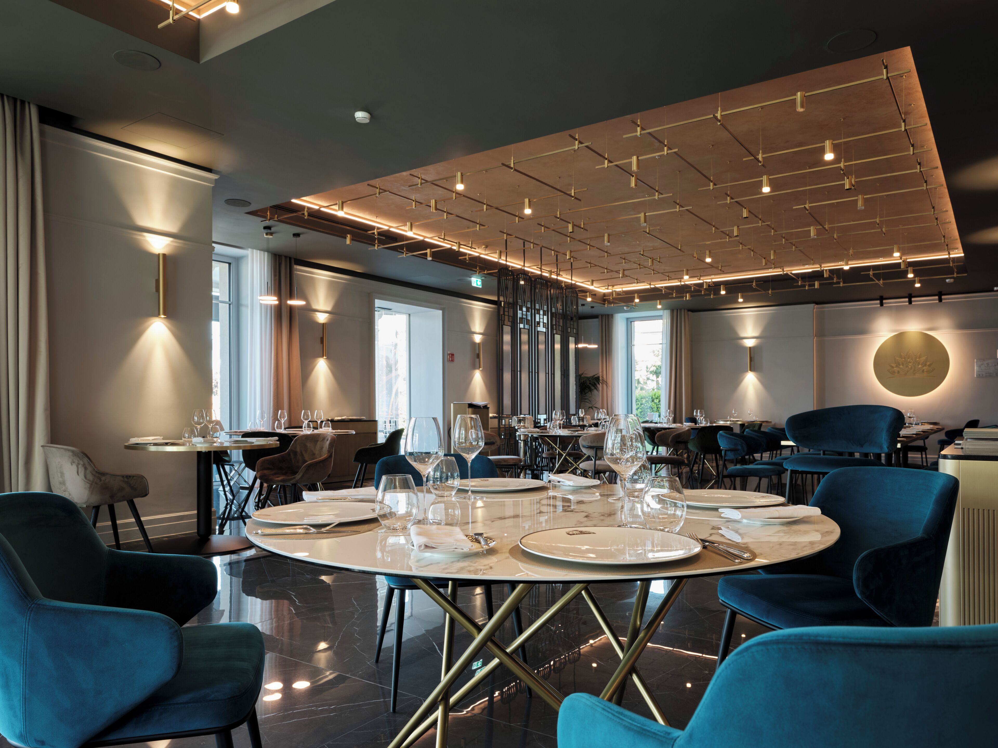 A modern dining area with round tables, blue chairs, and a ceiling with exposed beams and lighting fixtures.