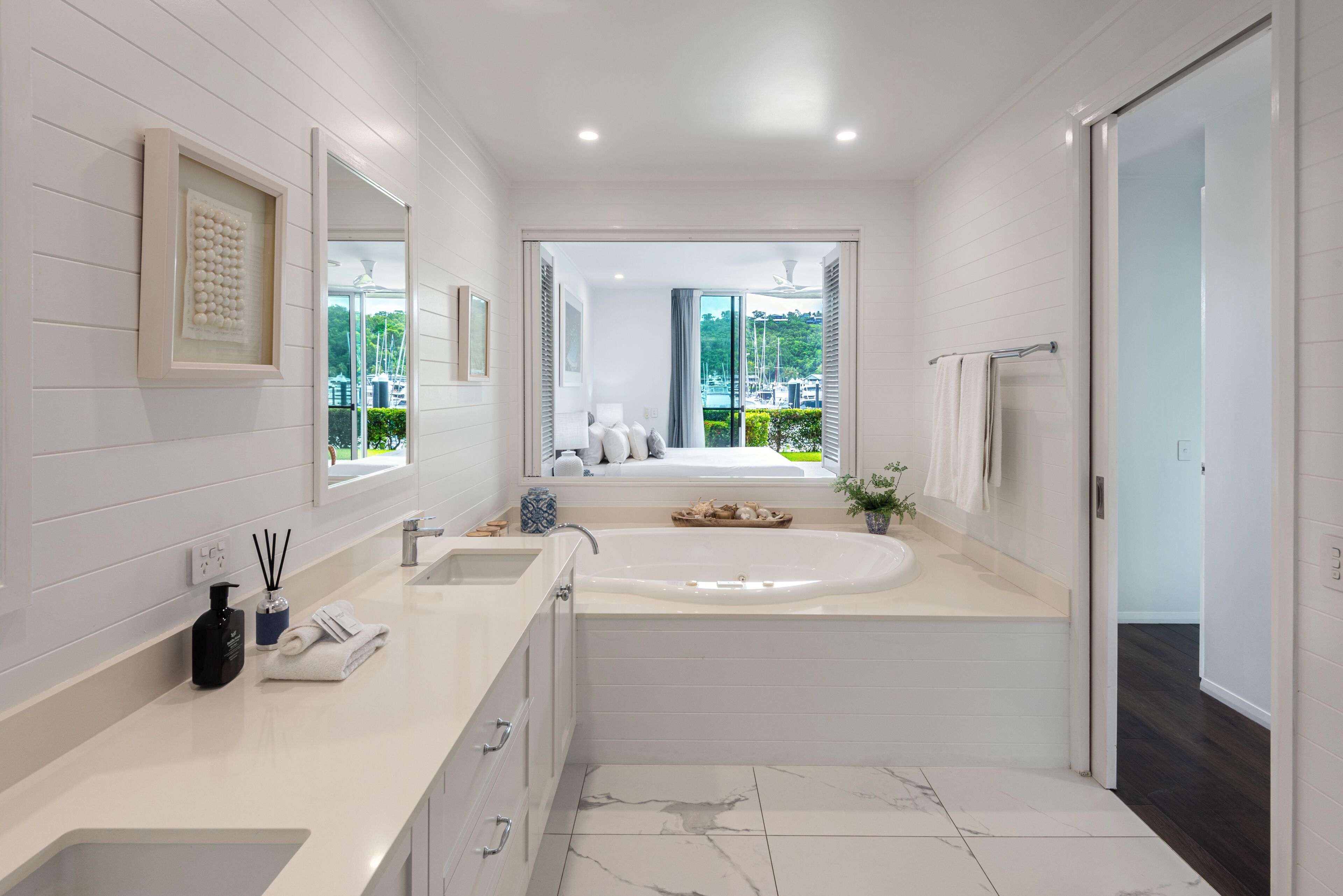 A modern bathroom with a large bathtub, a double sink, and a view of a marina.