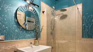 Casa de banho com lavatório, espelho, chuveiro e azulejos decorativos.