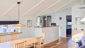 Eine moderne Küche mit einer zentralen Kochinsel, einem Holztisch mit Stühlen und Blick ins Freie.