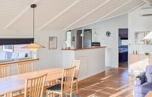 A modern kitchen with a central island, wooden dining table with chairs, and a view of the outdoors.
