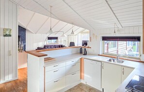 A kitchen with white cabinets, a wooden countertop, a built-in dishwasher, and a window with a view of the outside.