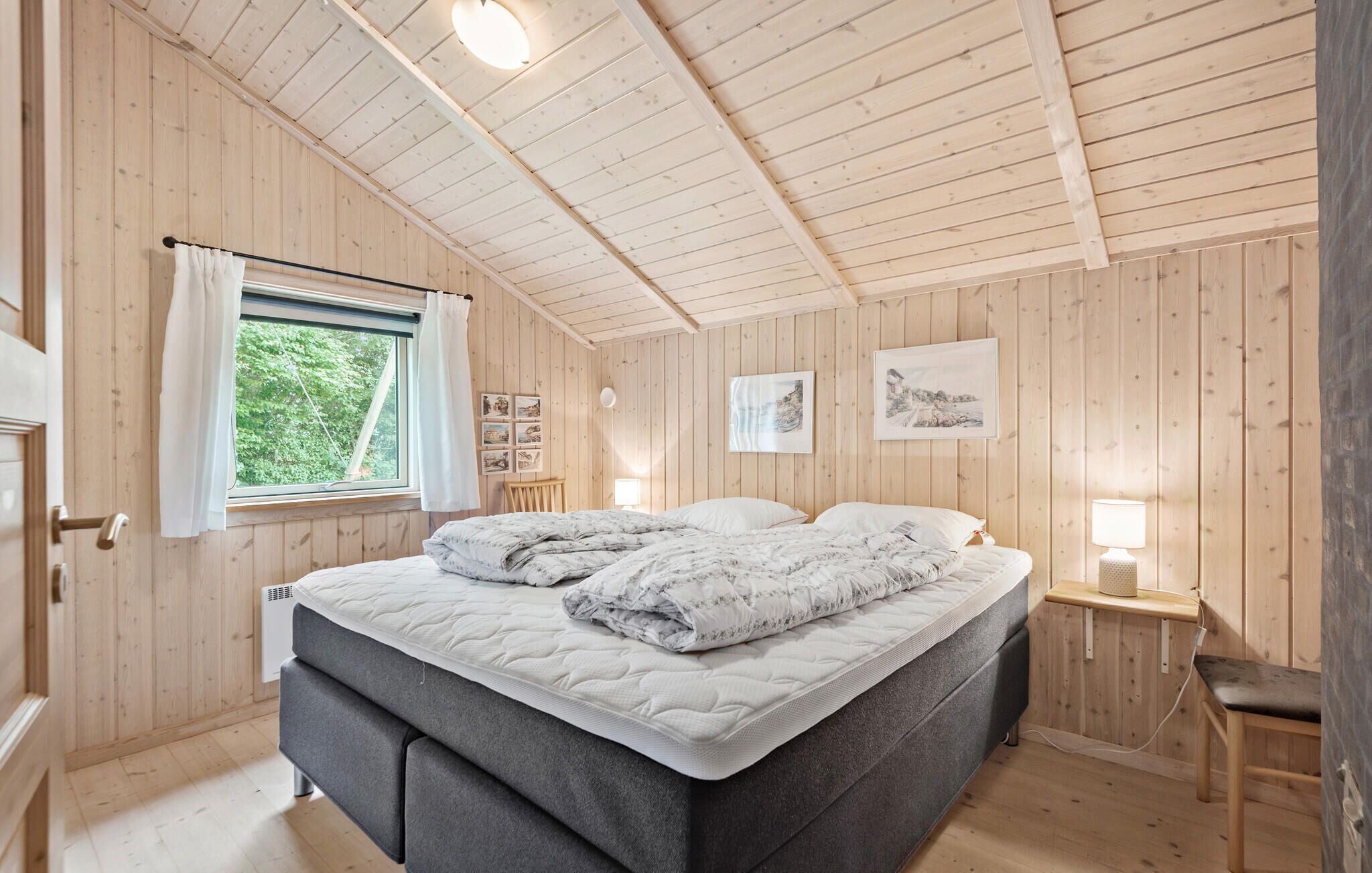 Een gezellige slaapkamer met een bed, een raam met gordijnen, een nachtkastje met een lamp en houten wanden.