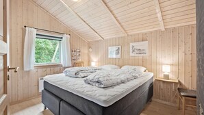 Ein gemütliches Schlafzimmer mit Bett, einem Fenster mit Vorhängen, einem Nachttisch mit Lampe und Holzwänden.