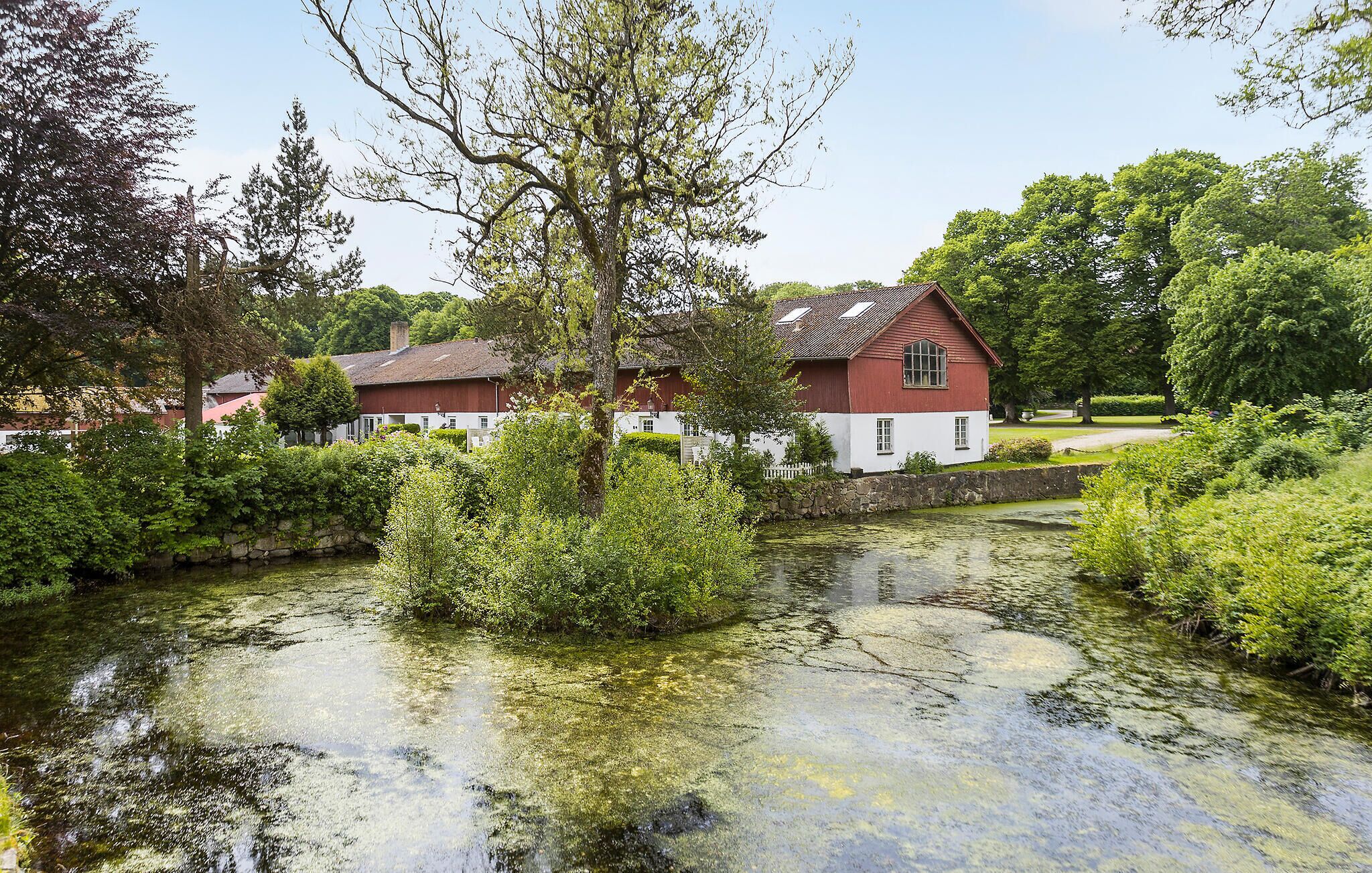 A traditional red and white house with a pond in front, surrounded by lush greenery.