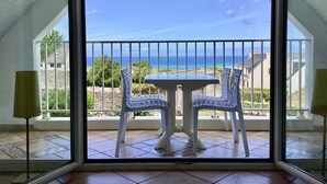 Een balkon met twee stoelen en een tafel, met uitzicht op de kust.