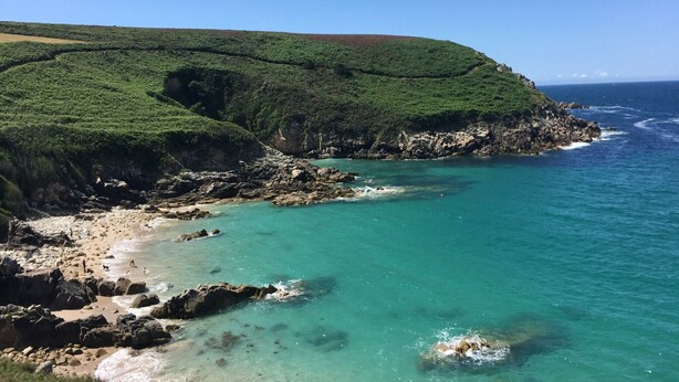 Een kustlandschap met een rotsachtig strand, helder turquoise water en een groene heuvel.