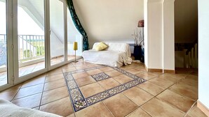 Een slaapkamer met een grote schuifglazen deur die uitkomt op een balkon, een bed met een witte hoes, een decoratief tapijt en een plant in een pot.