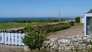 Une propriété située sur la côte, dotée d’un mur en pierre, d’une clôture blanche et offrant une vue sur la mer.