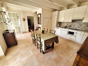 Zona pranzo con tavolo e sedie, cucina con mobili bianchi e forno a microonde, e pavimento piastrellato.