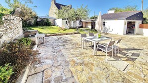 Eine Steinterrasse mit Gartenmöbeln, eine Steinsäule und ein kleiner Gartenbereich.