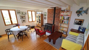 A cozy living room with a wooden floor, a dining table with chairs, a red sofa, a bookshelf, and a fireplace.