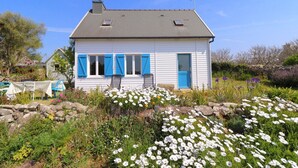 A white house with blue shutters, a stone wall, and a garden with white flowers.