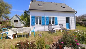 A white house with blue shutters, a small table, and two chairs in the front yard.