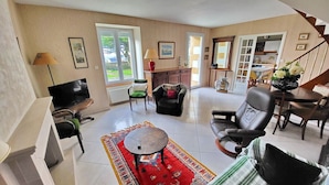 A spacious living room with a large window, a TV, a sofa, a dining table, and a staircase.