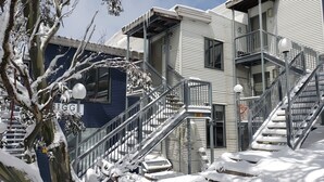 A multi-story building with a metal staircase and railings, surrounded by snow-covered trees. - Higgi Drive 5 - Mt Hotham (Hotham Heights)