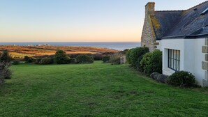 A white house with a stone chimney, a grassy yard, and a view of the sea.