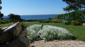 A garden with a view of the sea, featuring a variety of plants and a stone wall.
