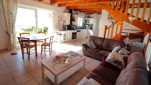 A spacious living area with a brown sofa, a dining table with chairs, and a kitchen in the background.