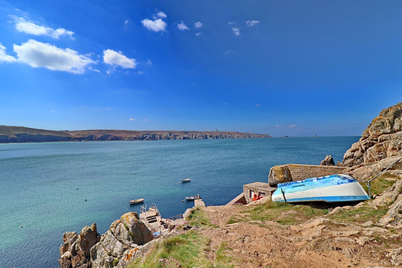 A coastal landscape with a clear blue sky, rocky terrain, and a body of water.