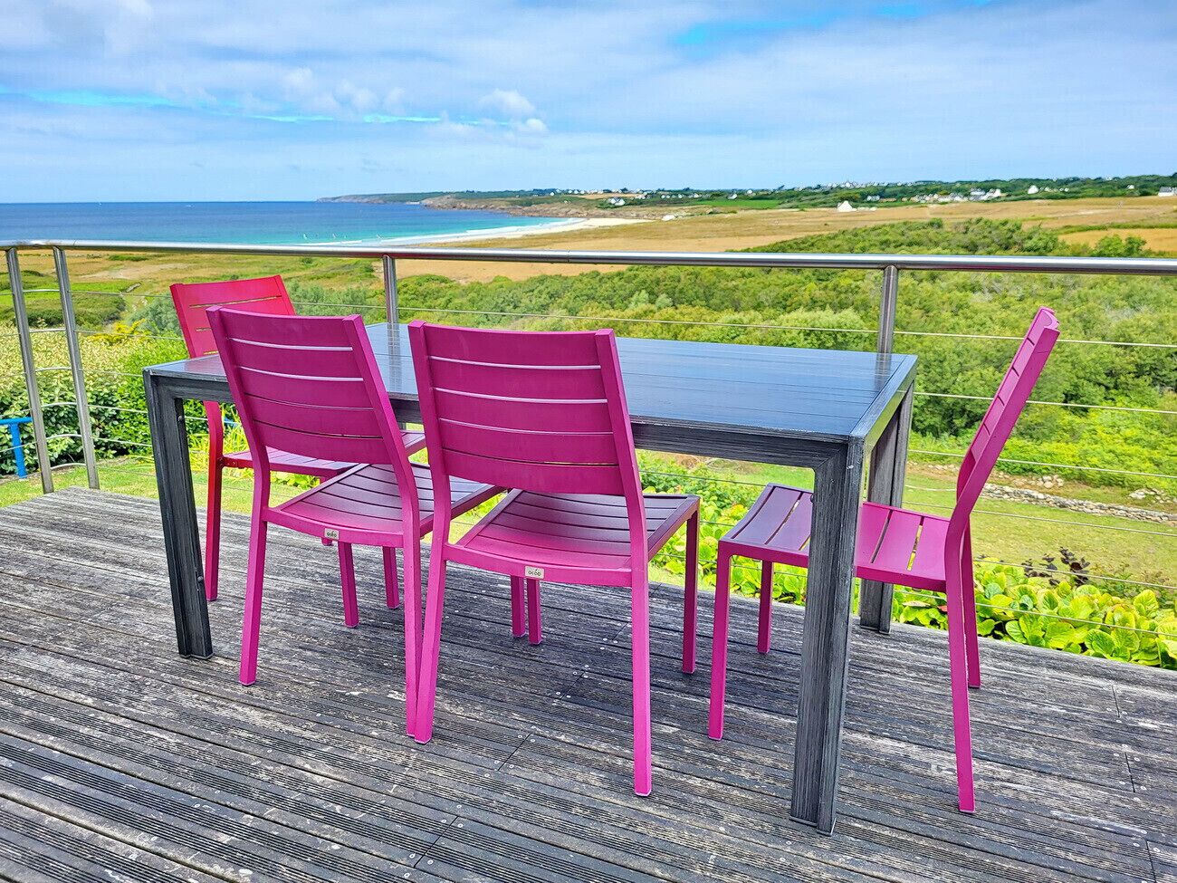 Una terraza de madera con una mesa y cuatro sillas, con vistas a un paisaje costero.