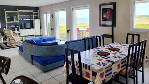 A spacious living area with a large window overlooking a beach, a dining table with chairs, and a blue sofa set. - 622-Ker An Enez,sea view, the beach at the end of the garden (Esquibien)