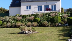 A two-story house with a sloped roof, a balcony with red chairs, and a stone wall in the foreground. - 622-Ker An Enez,sea view, the beach at the end of the garden (Esquibien)