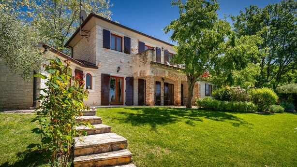 A two-story stone house with a covered porch and a well-maintained lawn.