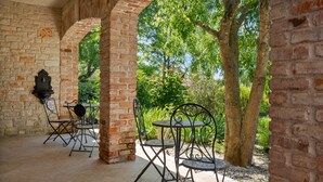 A covered patio with brick arches, outdoor tables and chairs, and a view of greenery.