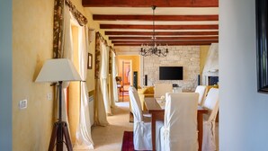 A dining area with a chandelier, a television mounted on a stone wall, and a fireplace.