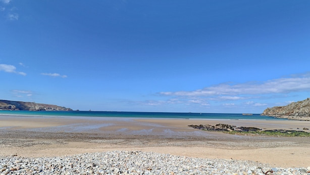 Una playa con piedras, una orilla de arena y un cielo azul despejado.